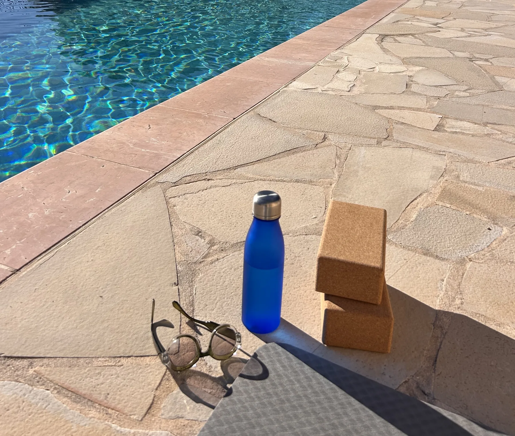 A mat, cork blocks and a water bottle resting in warm daylight beside a pool